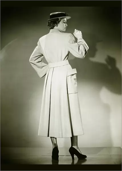 Woman in trench coat and hat posing in studio (Rear view), (B&W)