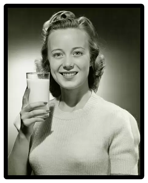 Smiling woman holding glass of milk in studio, (B&W), portrait