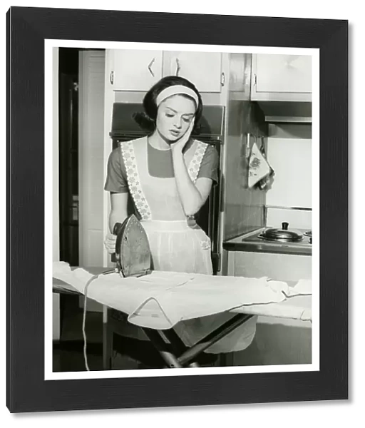 Young woman ironing in kitchen, (B&W)