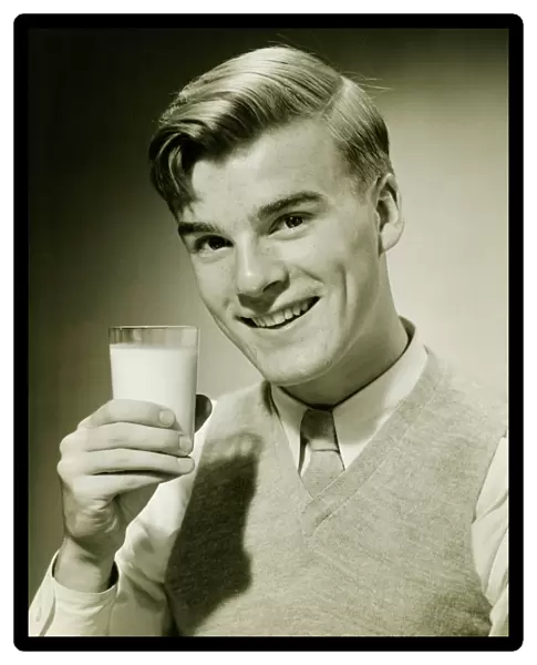 Young man holding glass of milk, smiling, (B&W), portrait
