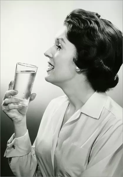 Woman holding glass of water, posing in studio, (B&W), (Portrait)