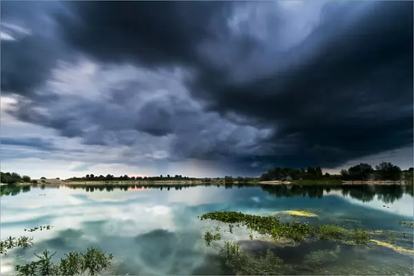Storm clouds over a quarry lake with water plants, near Mindelheim, Unterallgau, Allgau, Bavaria, Germany