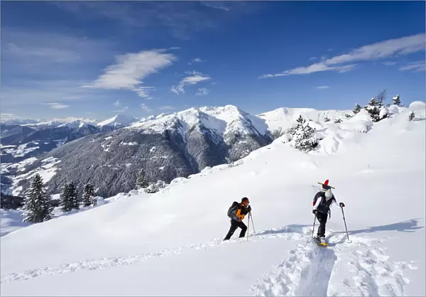 Snowshoe walkers during the ascent of the Mt Morgenrast summit from Unterreinswald, Sartntal valley and its mountains at back, South Tyrol, Italy, Europe
