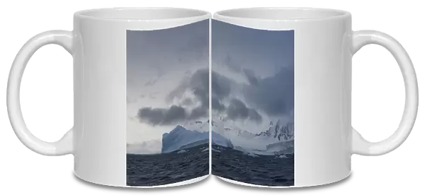 Iceberg in a fjord with mountain scenery and a cloudy sky, Gerlache Strait, Antarctic Peninsula, Antarctica