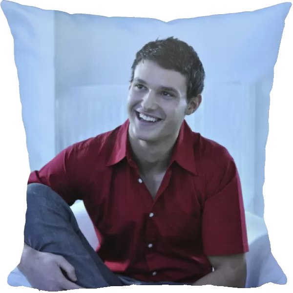 Young man wearing a red shirt sitting in an armchair, smiling