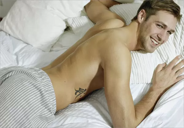 Charming bare chested man wearing pyjamas lying in bed, smiling