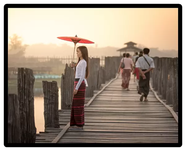 Beautiful woman holding traditional red umbrella and walking on U Bein Bridge, Myanmar