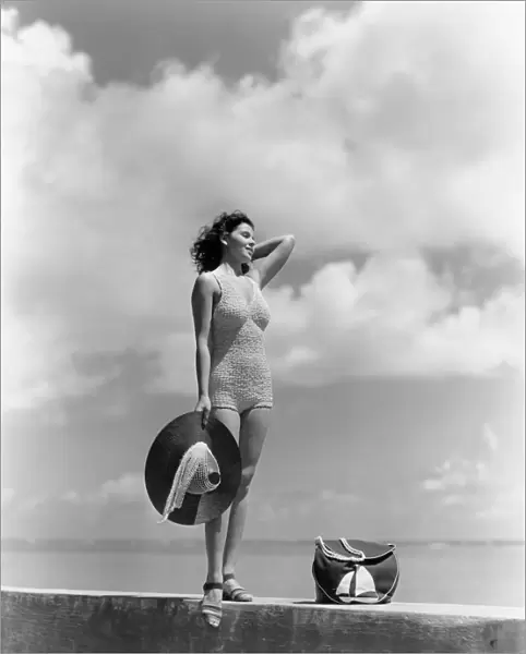 Woman Wearing Knit Bathing Suit Standing Wall Ocean Sea Background Holding Sun Hat Beach Bag Sail Boat Fashion Beauty Style Swim Wear Retro