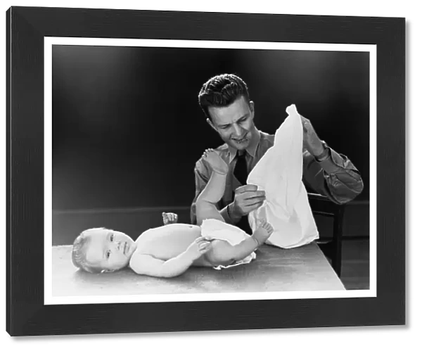 Young father with baby lying on table, trying to figure out how to put on diaper. (Photo by H