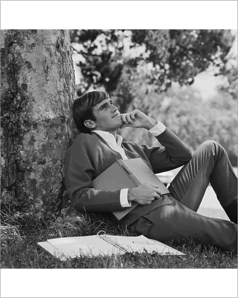Young man leaning against tree, holding book