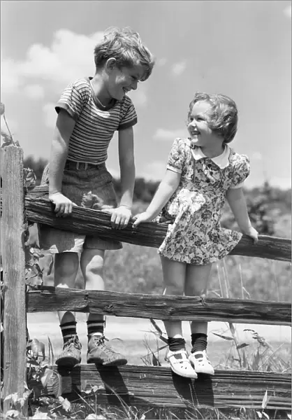 Boy and girl standing on split rail fence, looking at each other