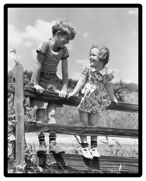 Boy and girl standing on split rail fence, looking at each other