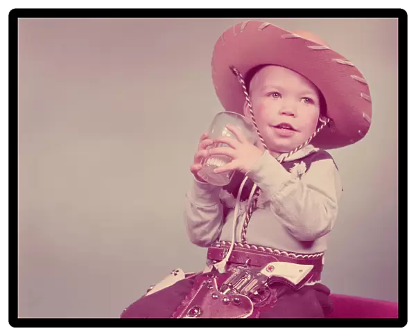 Toddler boy dressed as cowboy, drinking glass of milk. (Photo by H