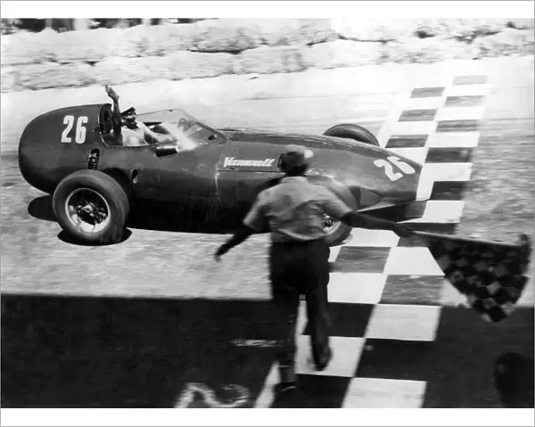 Stirling Moss raises his hand in salute as he crossed the chequered line to win the