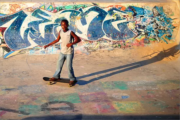 A young boy skateboards past a ramp decorated with graffiti in a skate park in Durban