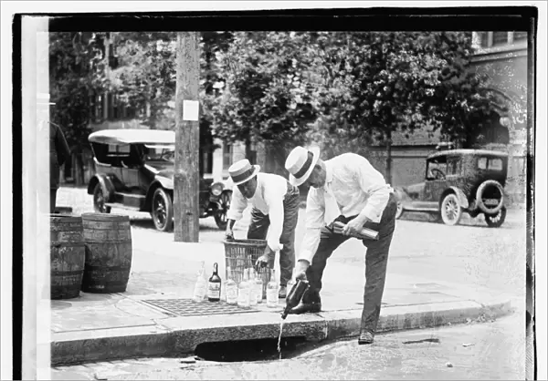 Two men pouring liquor into storm drain, 8 July 1921 (b  /  w photo)