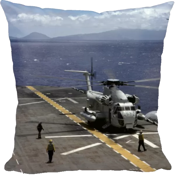 A CH-53D Sea Stallion sits on the flight deck as another prepares to land aboard