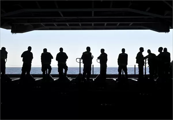 Silhouette of sailors standing in the hangar bay aboard USS Carl Vinson