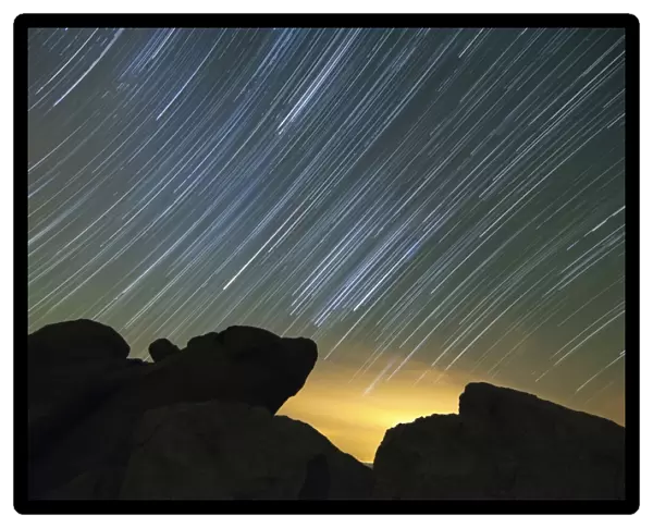 Light pollution illuminates the sky and star tails above large boulders