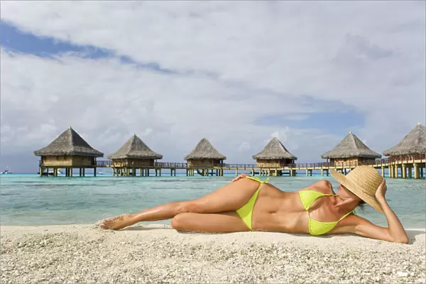 French Polynesia, Tuamotu Islands, Rangiroa Atoll, Woman Lounging On Beach, Luxury Resort Bungalows In Background