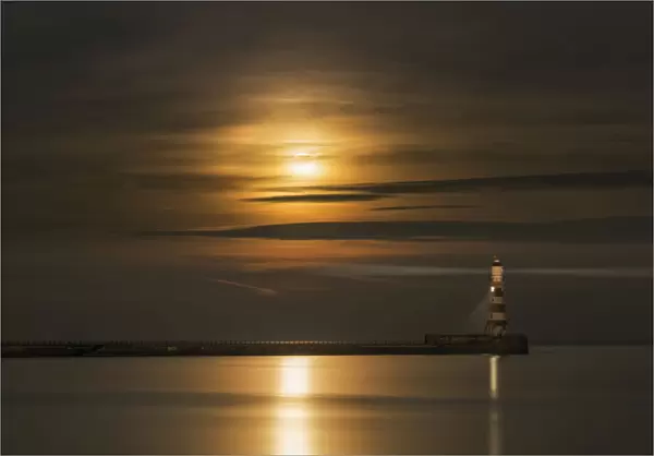Roker Lighthouse Casts A Light With The Golden Sunlight Shining Through Cloud And Reflecting On Tranquil Water; Sunderland, Tyne And Wear, England
