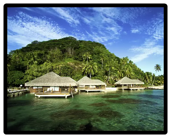 French Polynesia, Huahine, Te Tiare Resort Bungalows Over Ocean, Tall Palm Trees Along Beach, Blue Sky