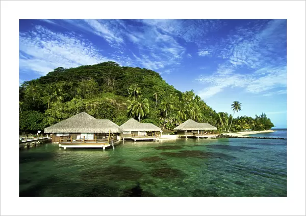 French Polynesia, Huahine, Te Tiare Resort Bungalows Over Ocean, Tall Palm Trees Along Beach, Blue Sky