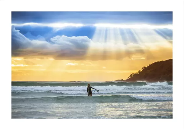 Surfer heading out to catch a wave at sunrise, Arrawarra, New South Wales, Australia