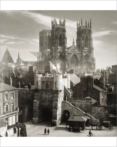 Historic image in sepia of York Minster Cathedral in the background and a typical victorian street scene with pedestrians and horse and carriage on the street, circa 1920; York, England
