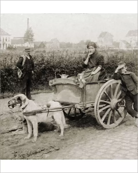 Historic image in sepia of a woman riding in a cart with milk jugs, and a boy and man standing by; Antwerp, Antwerp Province, Belgium