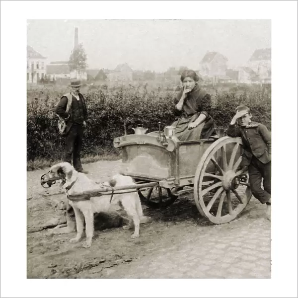 Historic image in sepia of a woman riding in a cart with milk jugs, and a boy and man standing by; Antwerp, Antwerp Province, Belgium