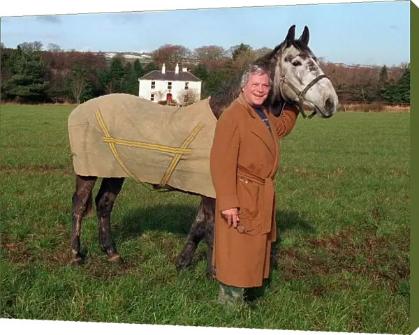 Oliver Reed actor wearing brown long coat standing in field with his horse Bobby at home