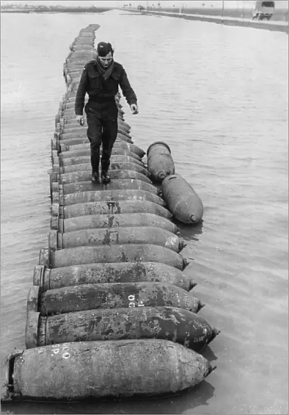 An airman using a line of 1000 lb bombs as a bridge to cross a flooded airfield at an RAF