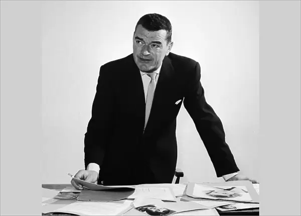 Actor Jack Hawkins looking at photographs on his desk April 1958