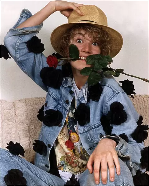 Emily Lloyd Actress sitting with hand on top of hat and with red rose in teeth