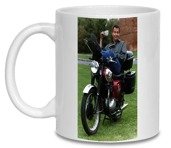 Michael Elphick actor sitting on motorbike holding cup of tea