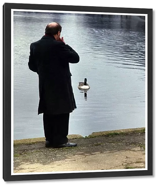 Gorden Kaye actor looking out over a boating lake in a park with duck paddling towards