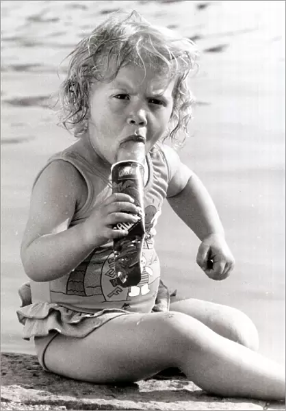 A young girl sits by a swimming pool, cooling off in the heat with a Ice Lolly. 1990