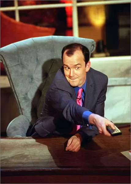 Jack Docherty sitting in chair left hand on desk right hand pressing television remote