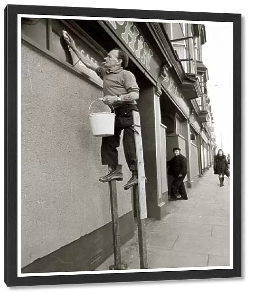 George Pettican Window Cleaner on Stilts cleaning windows on the front of his shop in