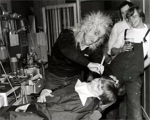A customer sits in the barbers chair having his faced shaved by a man in a mask at Steve