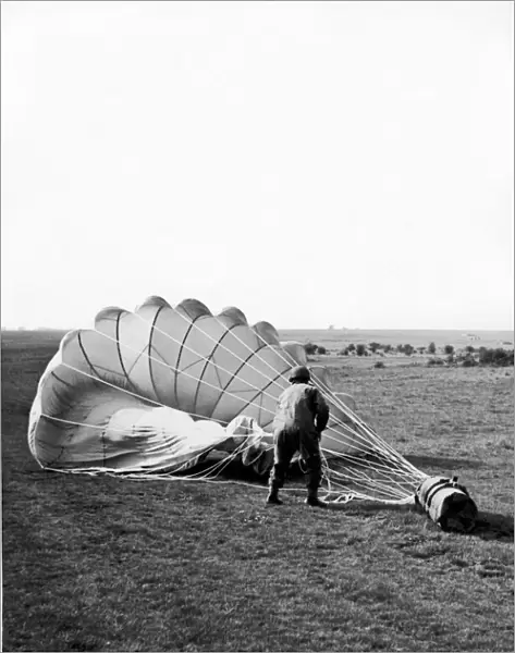 A paratrooper hauling in the parachute attached to a container which has been dropped