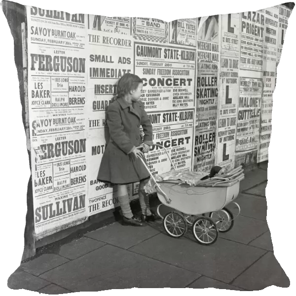 Little girl with toy pram stands waiting for her mother against a background of adverts