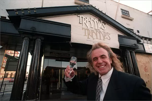 English nightclub owner Peter Stringfellow posing with a glass of champagne outside
