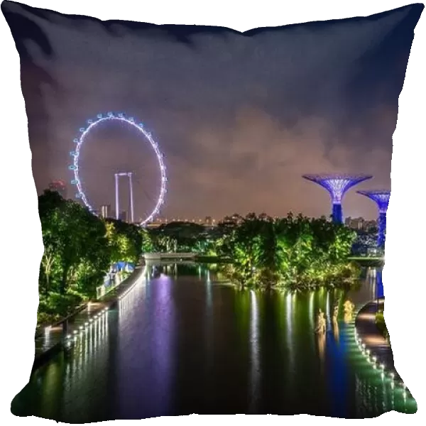 Supertree Grove forest in Gardens by the Bay illuminated with Singapore flyer ferris wheel at night. Asian tourism, modern city life, or business fina