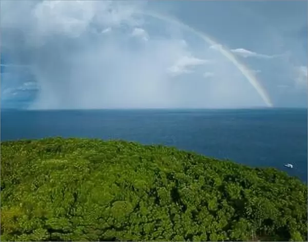 A bright rainbow appears behind a remote tropical island in the Solomon Islands. This beautiful country is home to spectacular marine biodiversity