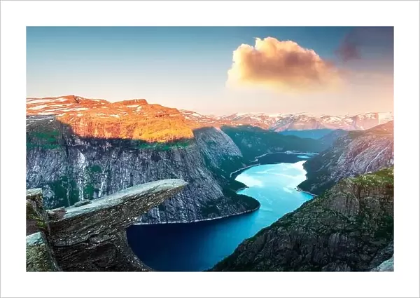 Breathtaking view of Trolltunga rock - most spectacular and famous scenic cliff in Norway. Picturesque landscape with sunset sky and clear lake