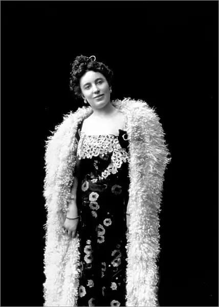 Three-quarter-length portrait of an actress from the Maresca Company. She is wearing a long dress, adorned with flowersand decorated with white lace, her bare shoulders are covered with a long white fur