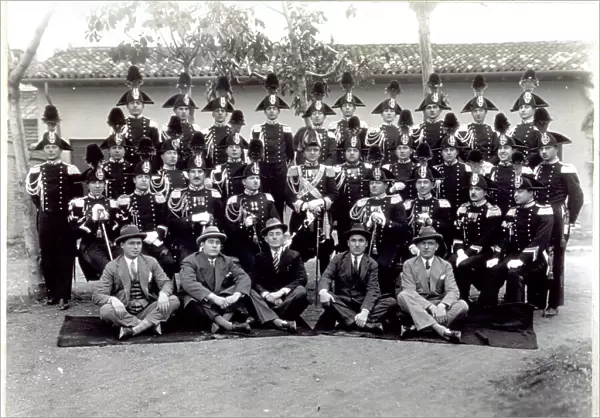 Portrait of a group of Carabinieri in full dress uniform. In the first row, sitting on the ground a group of five men in civilian clothes