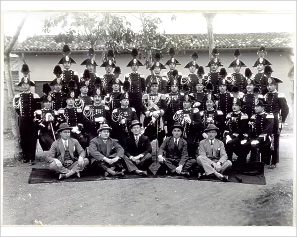 Portrait of a group of Carabinieri in full dress uniform. In the first row, sitting on the ground a group of five men in civilian clothes